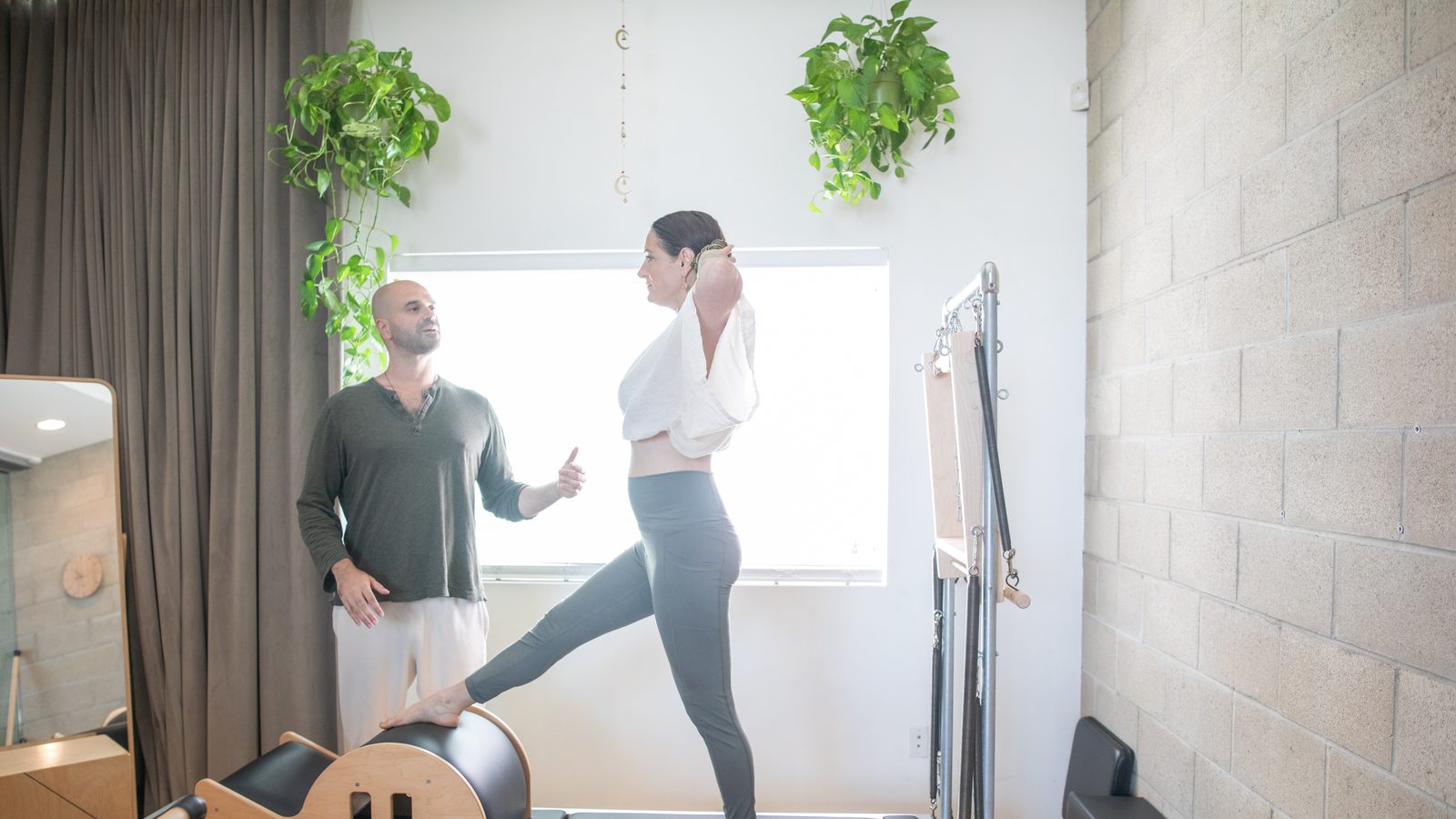 A teacher guiding a client through standing work on the reformer, one foot raised onto the barrel, during a private Pilates session at the West Hollywood studio.