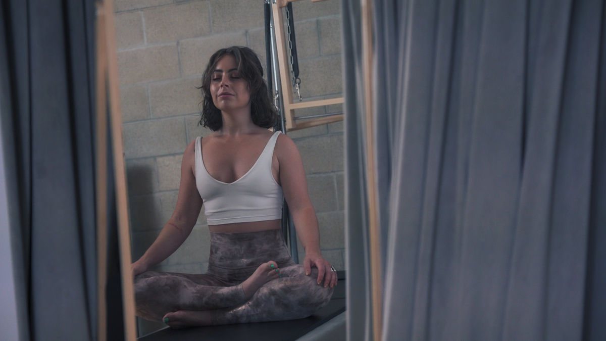 Woman centering into her breath before embarking on a detailed Pilates routine on a Contrology tower, reflecting the top-notch training provided at our Pilates Studio in West Hollywood.